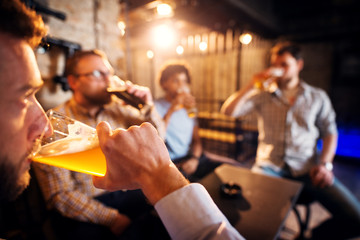 Close up view of man drinking beer while sitting in the pub with friends.