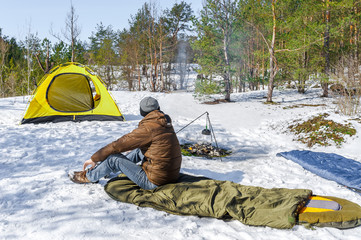 Climber arranges the sleeping pad in the bag near yellow tent in winter