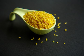 Croup of bulgur placer, pile on a black background lined in a spoon, a bowl. The product is rich in protein, healthy food, vegetarianism. View from above. Side view. Close up