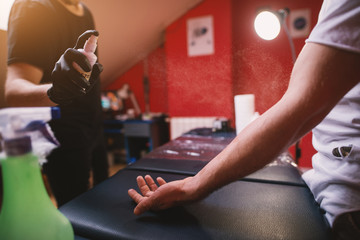 Tattoo artists spraying customers arm with spray for sterilization before further preparation for...