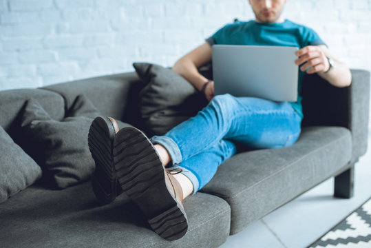 Cropped Shot Of Young Man Using Laptop On Sofa At Home