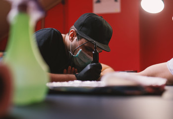 Young focused tattoo artist is inking customers arm carefully in