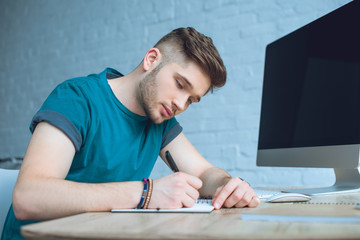 focused young man writing in notebook while working at home office