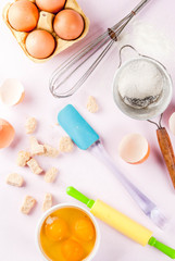 Ingredients and utensils for cooking baking egg, flour, sugar, whisk, rolling pin, on light pink background, top view