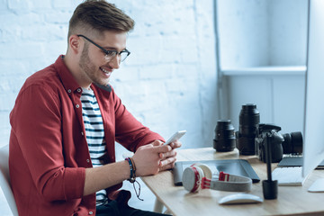 Happy freelancer man using smartphone sitting by working table