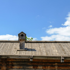 Old wooden rustic roof and chimney with birdhouse on the sky background. Square.