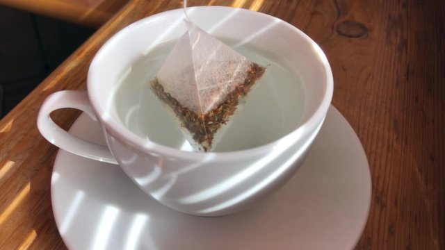 Tea bag with herbal tea being put into a white cup of hot water 