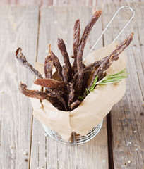 jerked meat, cow, deer, wild beast or biltong in kraft paper bowls on a rustic table, selective...
