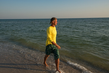 Joyful adventurer is walking along the surf line during sunset