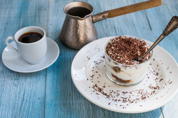 Homemade Italian dessert tiramisu in a glass with grated chocolate, and a cup of coffee on a rustic table, copy space