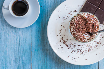 Homemade Italian dessert tiramisu in a glass with grated chocolate, and a cup of coffee on a rustic table, copy space