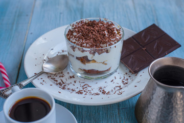 Homemade Italian dessert tiramisu in a glass with grated chocolate, and a cup of coffee on a rustic table