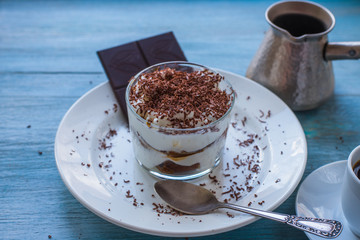 Homemade Italian dessert tiramisu in a glass with grated chocolate, and a cup of coffee on a rustic table