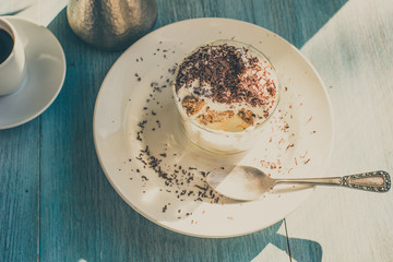Homemade Italian dessert tiramisu in a glass on the table in the early morning - a rustic breakfast