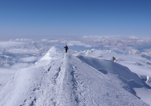 male back country ski mountaineer hiking along a narrow and exposed summit ridge of a high alpine peak