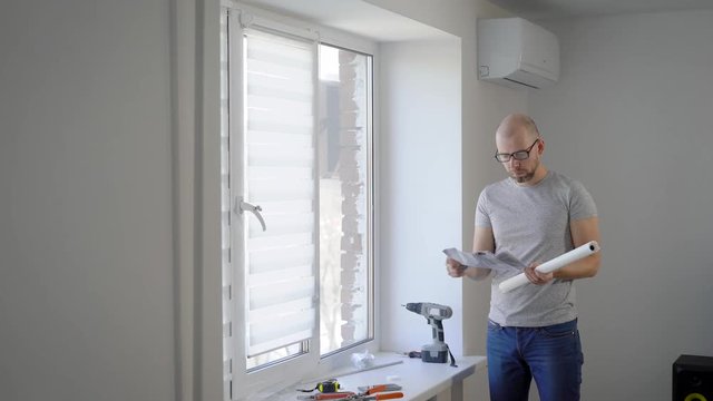 young man is arranging details for installing white protective curtains on windows in a bedroom in daytime