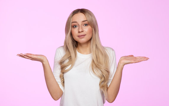 Studio portrait of cute puzzled young woman shrugs shoulders, does not know what happened. Pretty woman doubting isolated on pink background