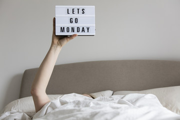 Female in bed under the sheets holding up a lets go monday sign
