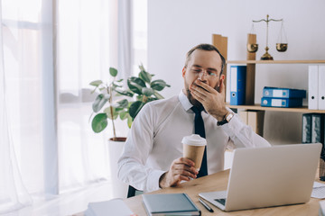 portrait of tired lawyer with coffee to go yawning at workplace in office - obrazy, fototapety, plakaty