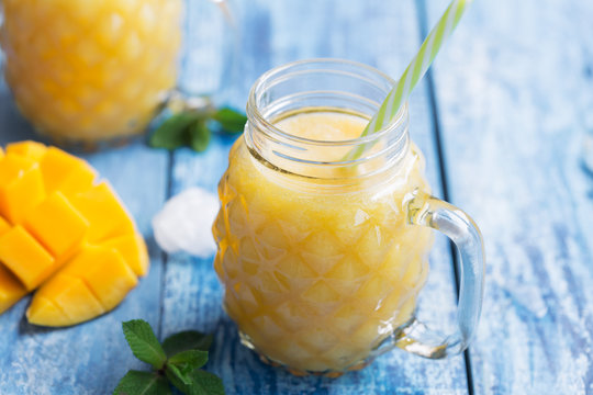 Fresh mango smoothie with ice and pepper mint on a blue wooden rustic background. close up