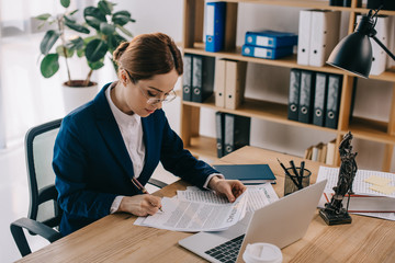 side view of female lawyer doing paperwork at workplace with laptop in office