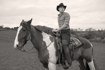 Cowboy wearing chequered shirt and hat riding horse , on horseback