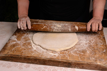 An old grandmother cleansing a dough with a shaft on a dark background