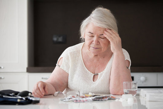  A gray-haired woman holds her head while sitting at a table.