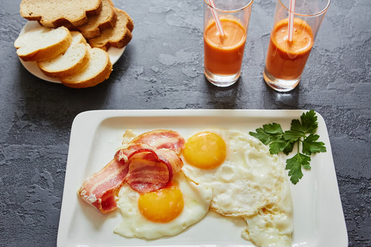 Daily Breakfast. Fried egg with bacon, carrot juice, vegetable salad, bread. On dark stone background