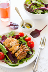 Sliced grilled chicken with green leaves salad on white plate