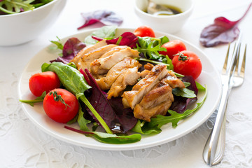 Sliced grilled chicken with green leaves salad on white plate