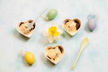 Fototapeta na wymiar Traditional Finnish Easter pudding, Mammi, rye pudding with Vanilla cream in Heart shaped Ceramic dish and pastel color ceramic spoon on blue background with Easter decorations, top view