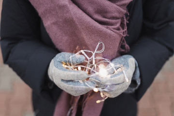Woman in woolen gloves holding led lights. Christmas spirit and magic