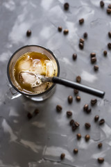 Black cold coffee with ice and milk on a gray background among the coffee beans. Summer cooling drink in a glass cup. Top view, flat lay