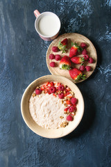 Sweet rice porridge pudding in ceramic plate with berries strawberry and raspberry, walnuts, mug of milk over blue texture background. Top view, space.