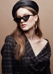 Fashion portrait of beautiful young woman in black leather beret cap, plaid jacket and cat eye...