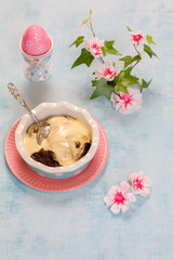 Traditional Finnish Easter pudding, Mammi, rye pudding with Vanilla cream in Heart shaped Ceramic dish and pastel color ceramic spoon on blue background with Easter decorations, top view