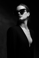 Fototapeta premium Sexy elegant black and white portrait of young beautiful woman in black deep v neck jacket and dark sunglasses