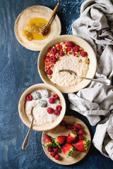 Sweet rice porridge pudding in ceramic plate with berries strawberry and raspberry, walnuts, honey on cloth over blue texture background. Top view, space.