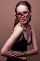 Fashion portrait of beautiful young woman in black bra, sunglasses with red lens, with massive...