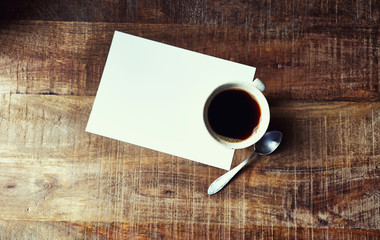 Mug of Black Coffee and a blank paper sheet on rustic wooden table; seen from above