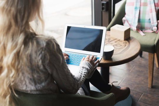 Young fashion woman working on her laptop and sitting at the table and drinking coffee in cafe. Stylish female model with blonde hairs