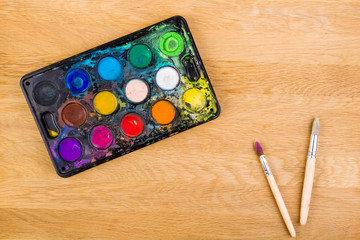 Box with watercolors and brushes on wooden surface