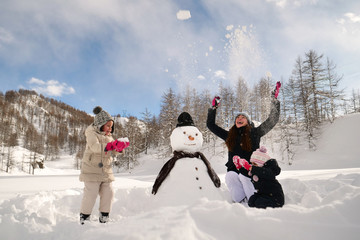 On a winter day, on the mountains with snow, a family plays with a snowman. Concept of: winter holidays, family, christmas, mountain