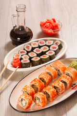 Different  sushi rolls with rice, vegetable, seafood on ceramic plates, glass bottle with soy sauce and red pickled ginger in a bowl
