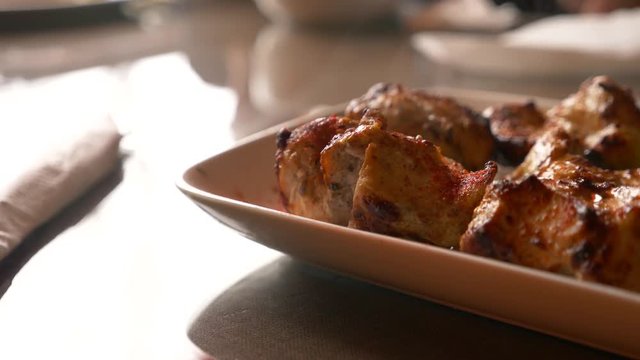 Close of roasted meat lying on a white plate with greens on a table in slow motion, 4k, steam from hot meat