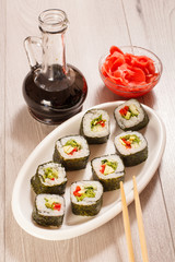 Sushi rolls with rice on ceramic plate, chopsticks, glass bottle with soy sauce and pickled ginger in a bowl