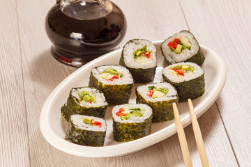 Sushi rolls with rice, pieces of avocado, cucumber and lettuce leaves on ceramic plate, glass bottle with soy sauce