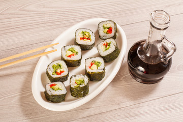 Sushi rolls with rice, pieces of avocado, cucumber and lettuce leaves on ceramic plate, glass bottle with soy sauce