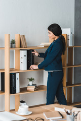 Businesswoman stacking folders on shelf in modern office